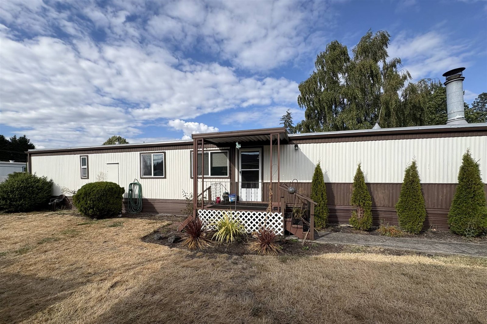 A manufactured home with dated brown trim and a dry, patchy lawn