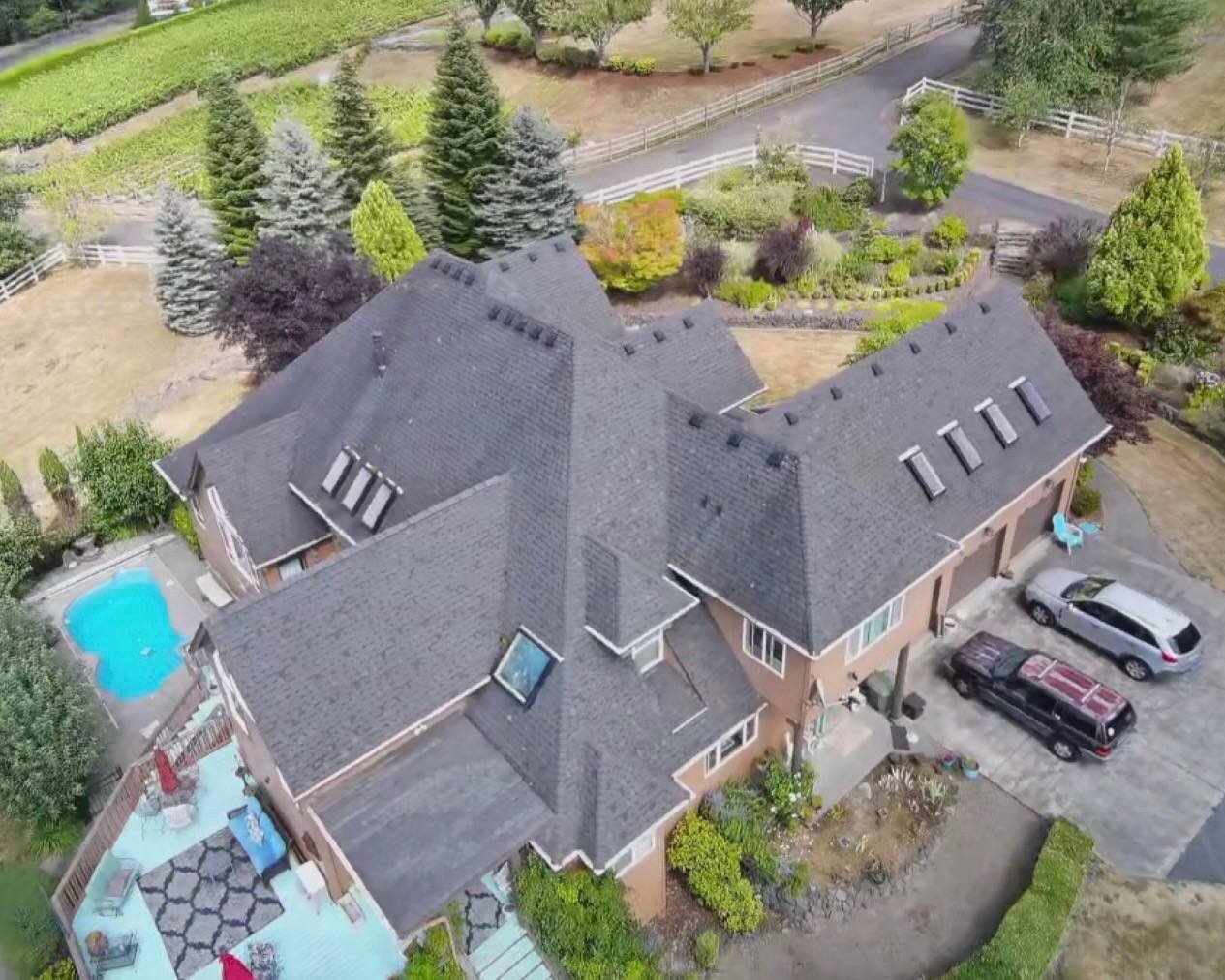 A large house photographed from above with its existing dark, weathered roof