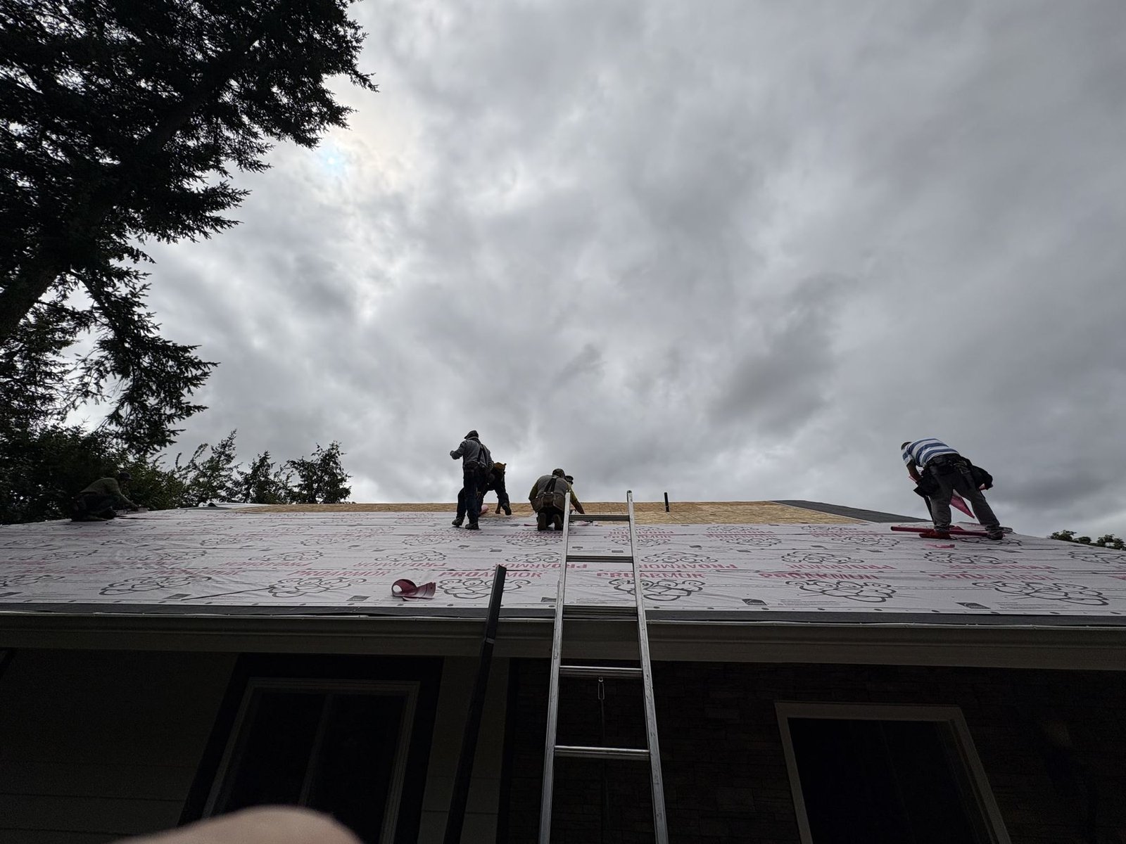 The crew on the roof with the underlayment down and a ladder at the eave
